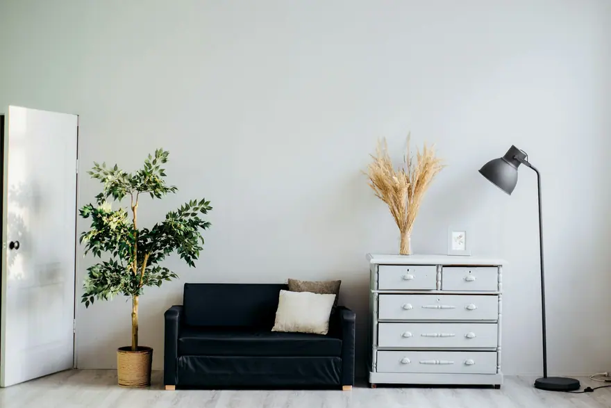 Room with light grey walls, a black loveseat, a white dresser and a floor lamp