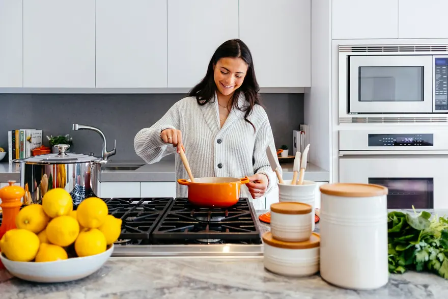 Person cooking at a gas cooktop in a white kitchen with a stone island